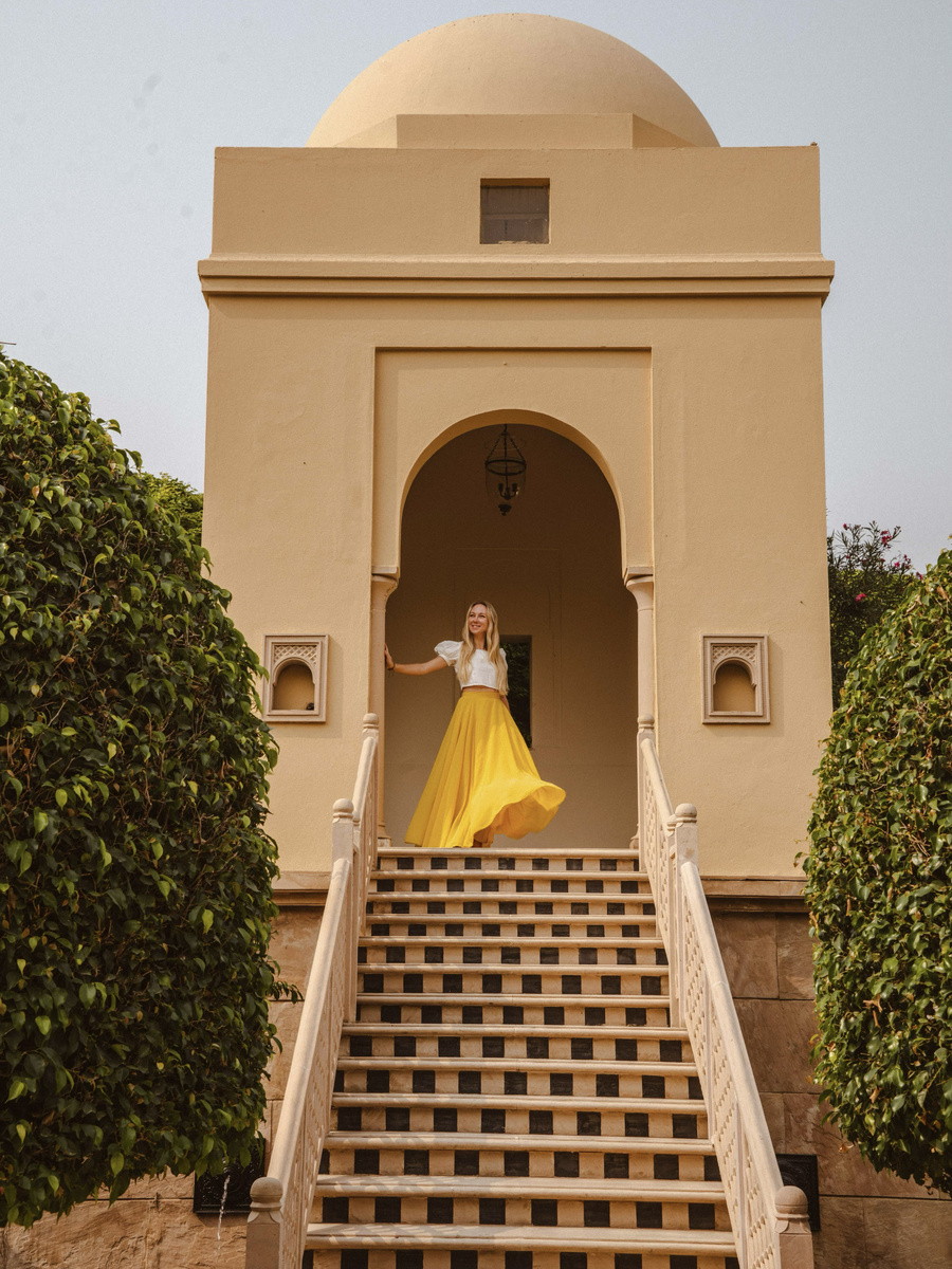 Olga in a yellow skirt stands at the top of a pavilion staircase in the gardens of The Oberoi Amarvilas.