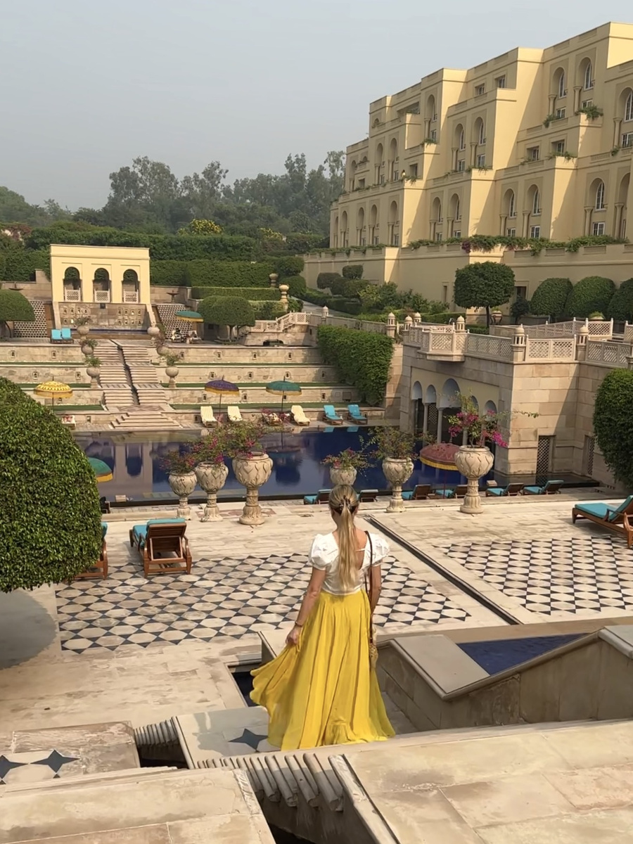 Olga in a yellow skirt walks down marble steps toward the pool and gardens at The Oberoi Amarvilas.