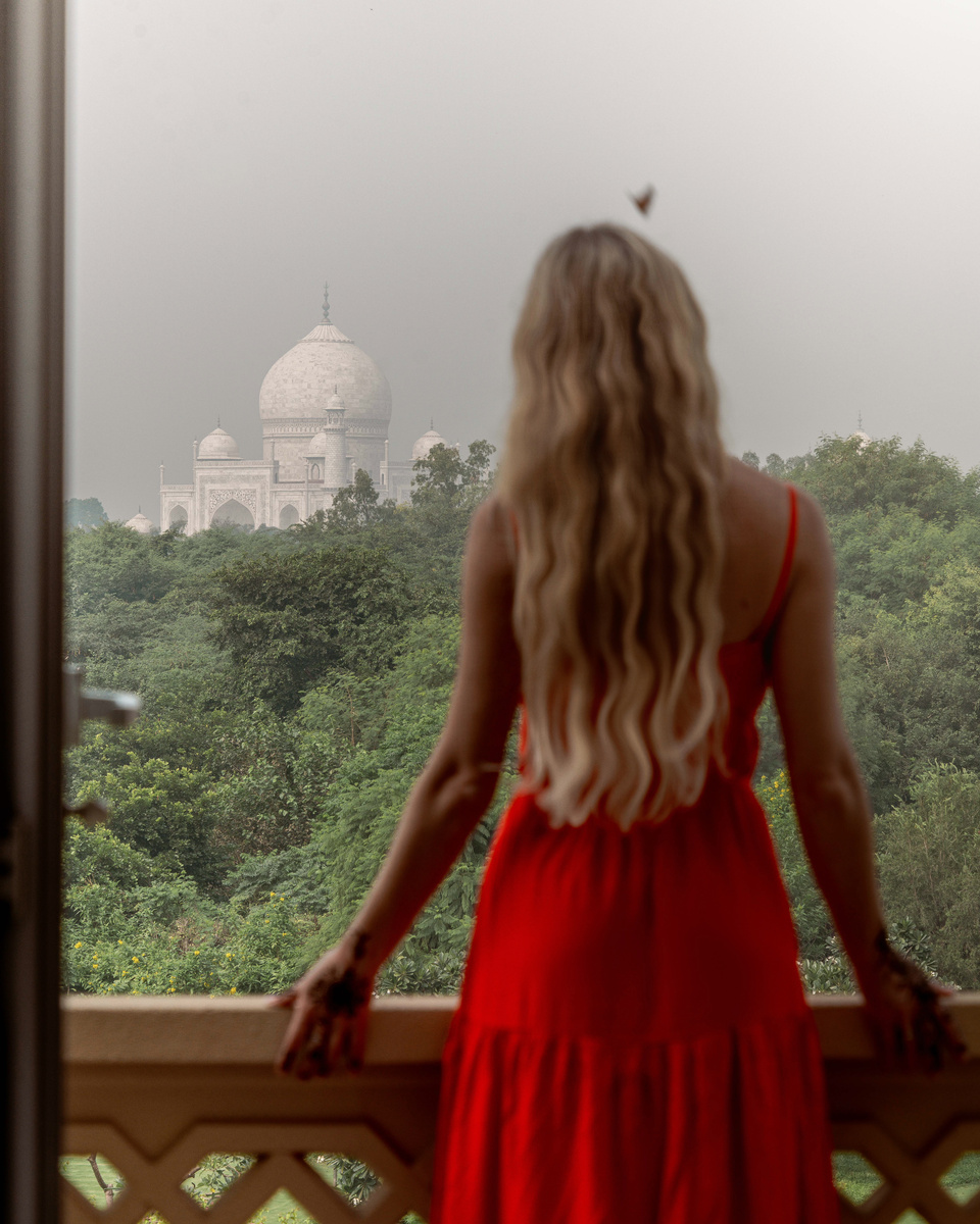 Olga in a red dress looks toward the Taj Mahal from a balcony at The Oberoi Amarvilas.