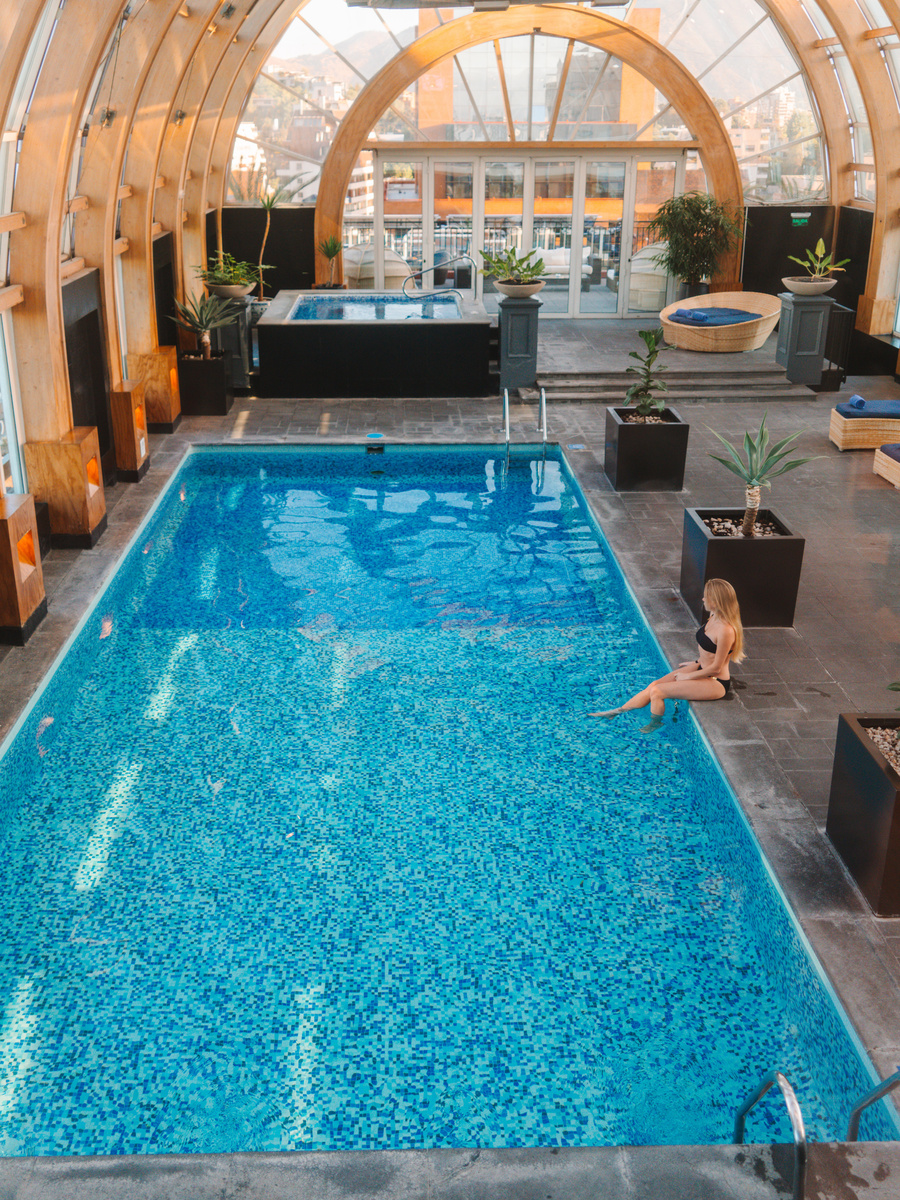 The long indoor pool at The Ritz-Carlton Santiago rises beneath a tall curved glass roof.