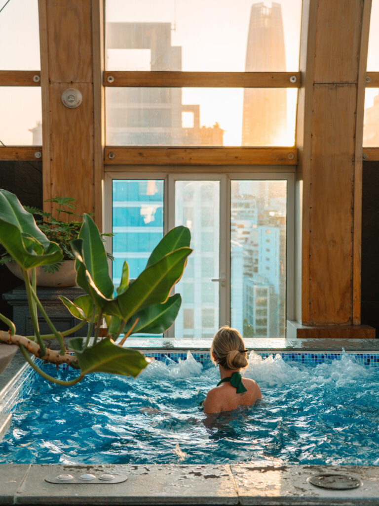 Olga stands beside the rooftop pool at The Ritz-Carlton Santiago as sunset colours the glass roof and city skyline.
