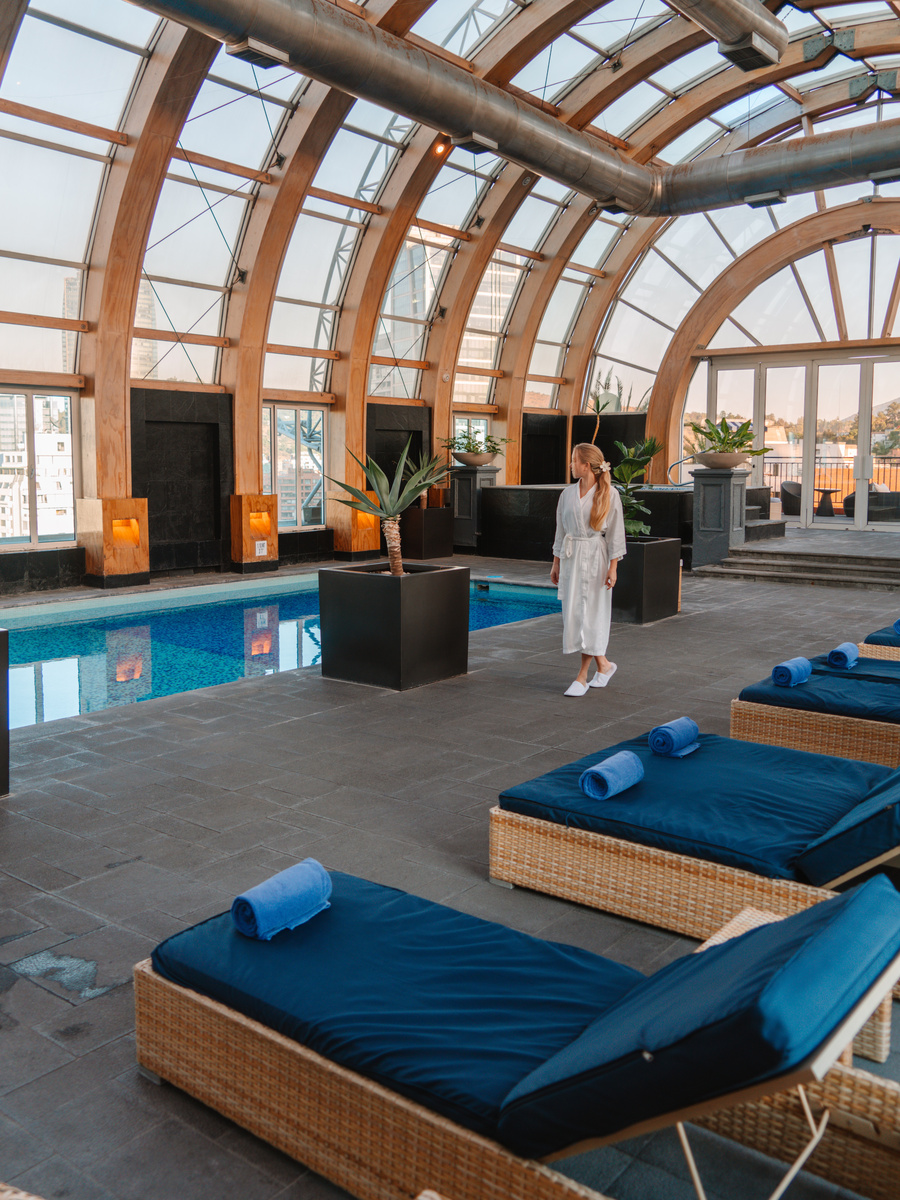 Olga walks beside the indoor rooftop pool beneath the curved glass roof at The Ritz-Carlton Santiago.