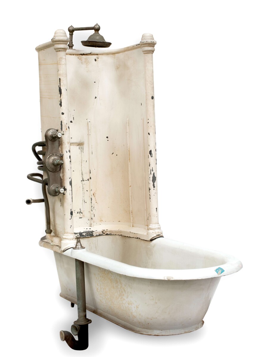 White enamelled late-nineteenth-century bathtub from the Ritz Paris, with a tall curved splashback, overhead shower and exposed valves.