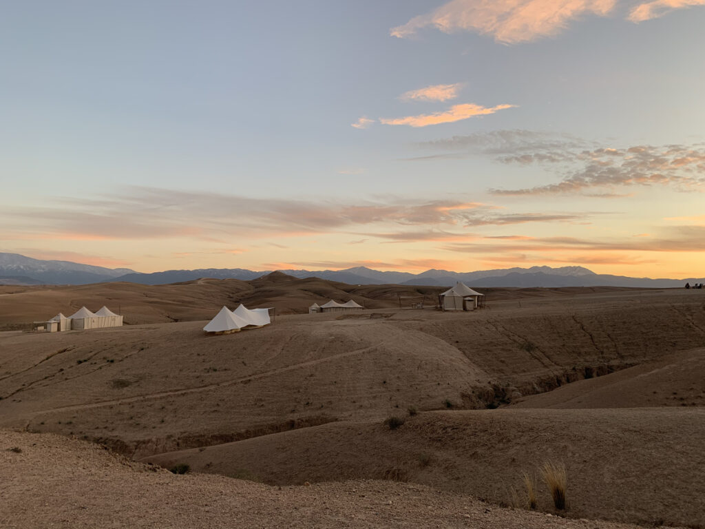 Scarabeo Camp tents across the rocky Agafay landscape at sunset, with the Atlas Mountains beyond