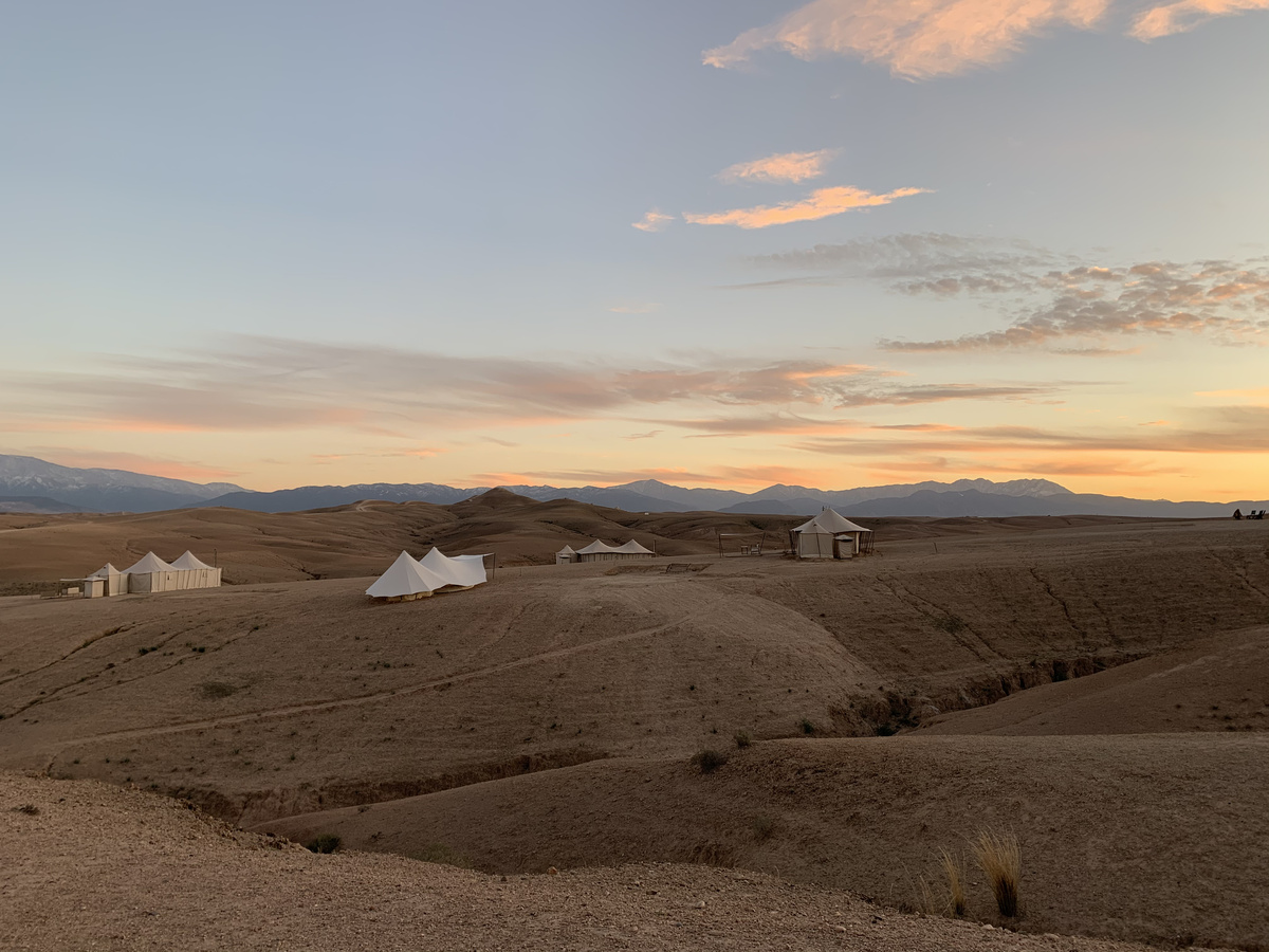 Scarabeo Camp tents across the rocky Agafay landscape at sunset, with the Atlas Mountains beyond