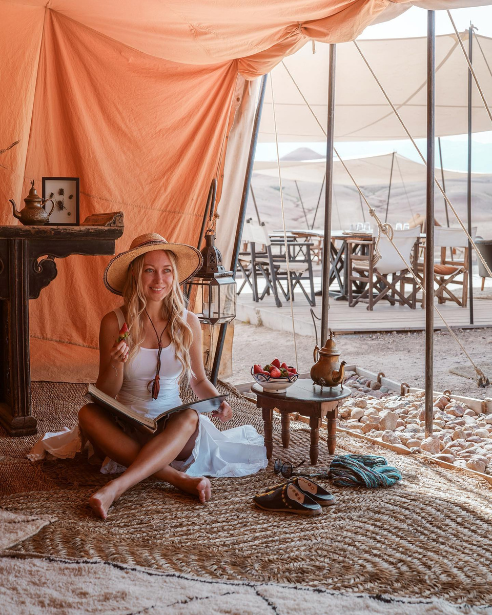 Olga sitting inside a canvas tent at Scarabeo Camp in Agafay, with tea, strawberries, woven rugs, and the camp outside