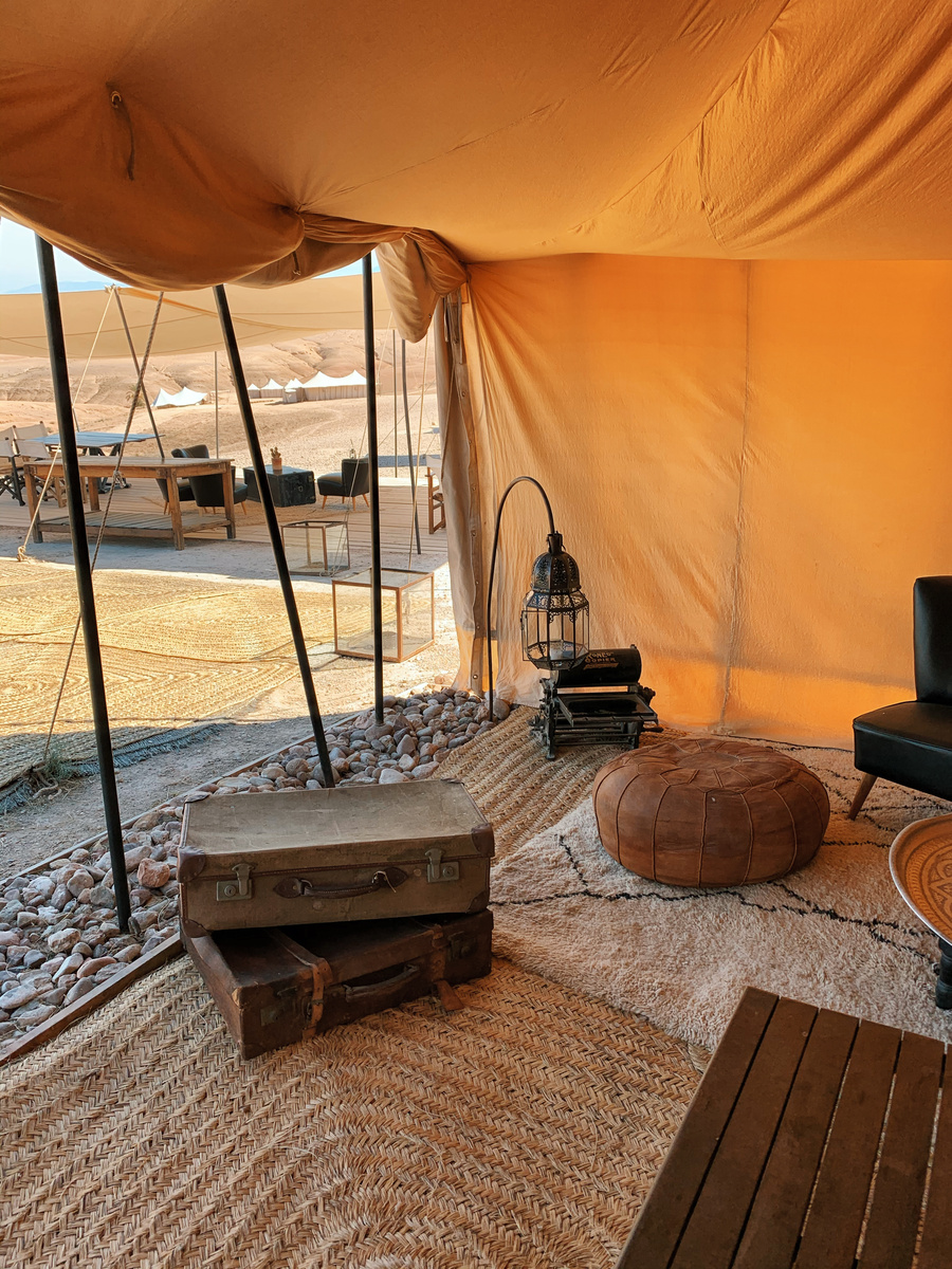 Warm canvas tent interior at Scarabeo Camp with old trunks, woven rugs, leather pouf and Moroccan lantern
