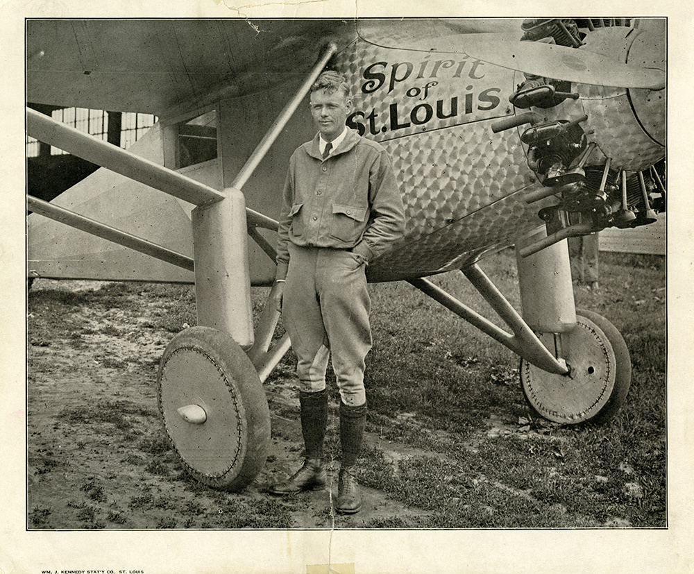 Charles Lindbergh stands beside the nose and landing gear of the Spirit of St. Louis in a 1927 black-and-white photograph.