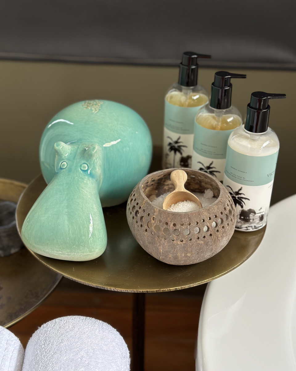A turquoise ceramic hippo, bath products and a bowl of shells sit in a tented-suite bathroom at Victoria Falls River Lodge.