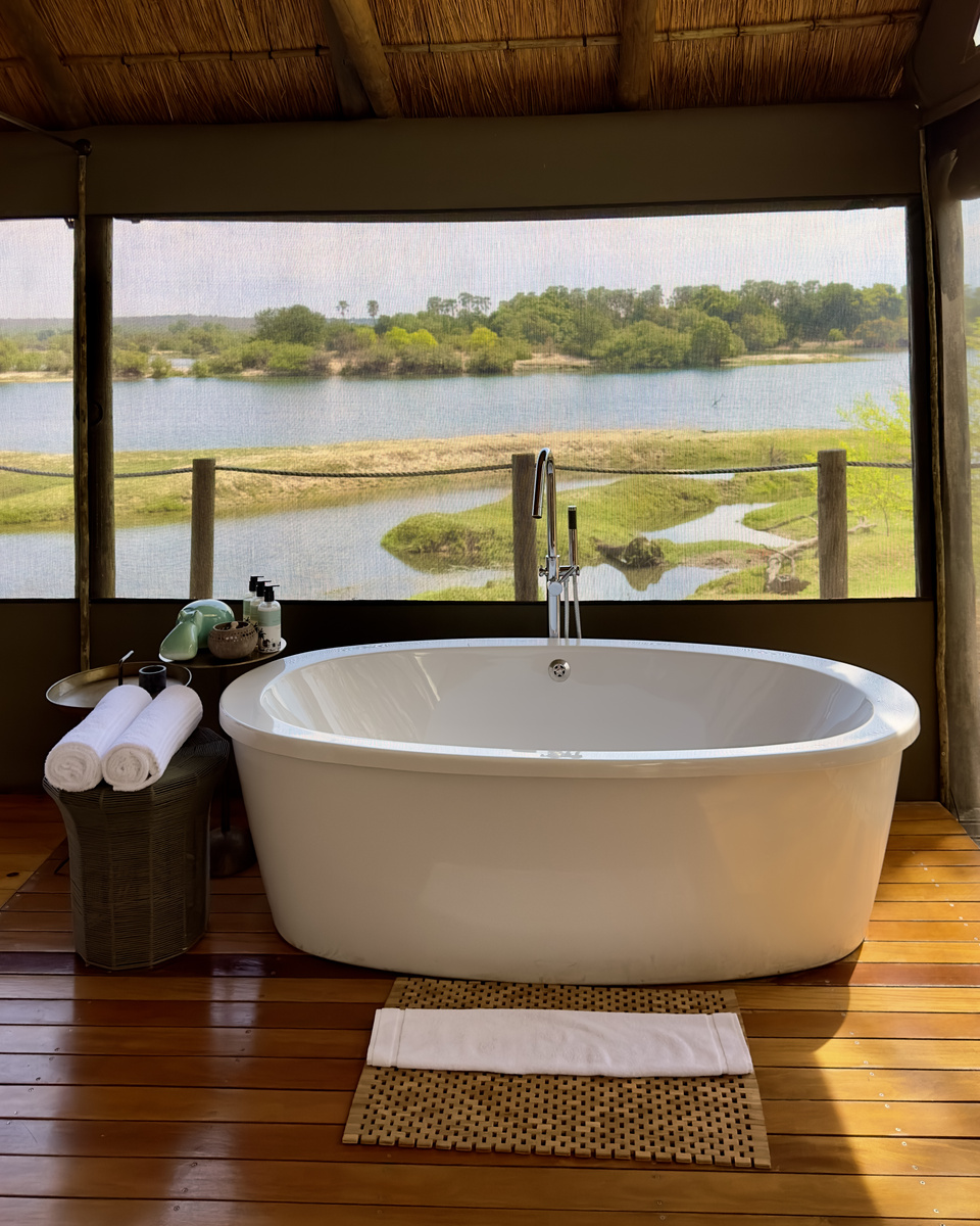 A freestanding white bathtub faces the Zambezi River through the mesh wall of a Victoria Falls River Lodge tented suite.