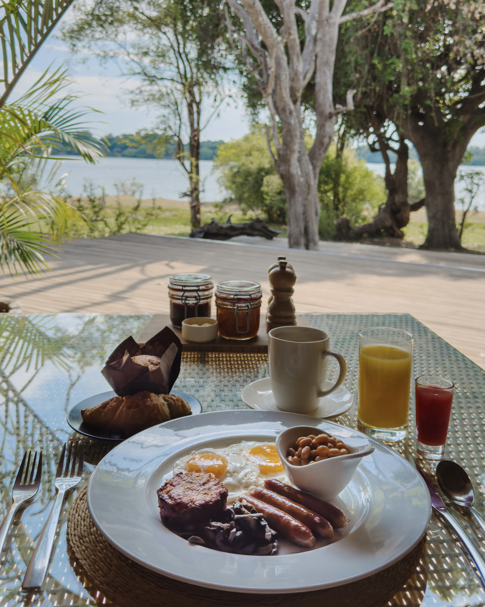 Eggs, bacon, mushrooms, bread, fruit and juice are served for breakfast overlooking the Zambezi at Victoria Falls River Lodge.