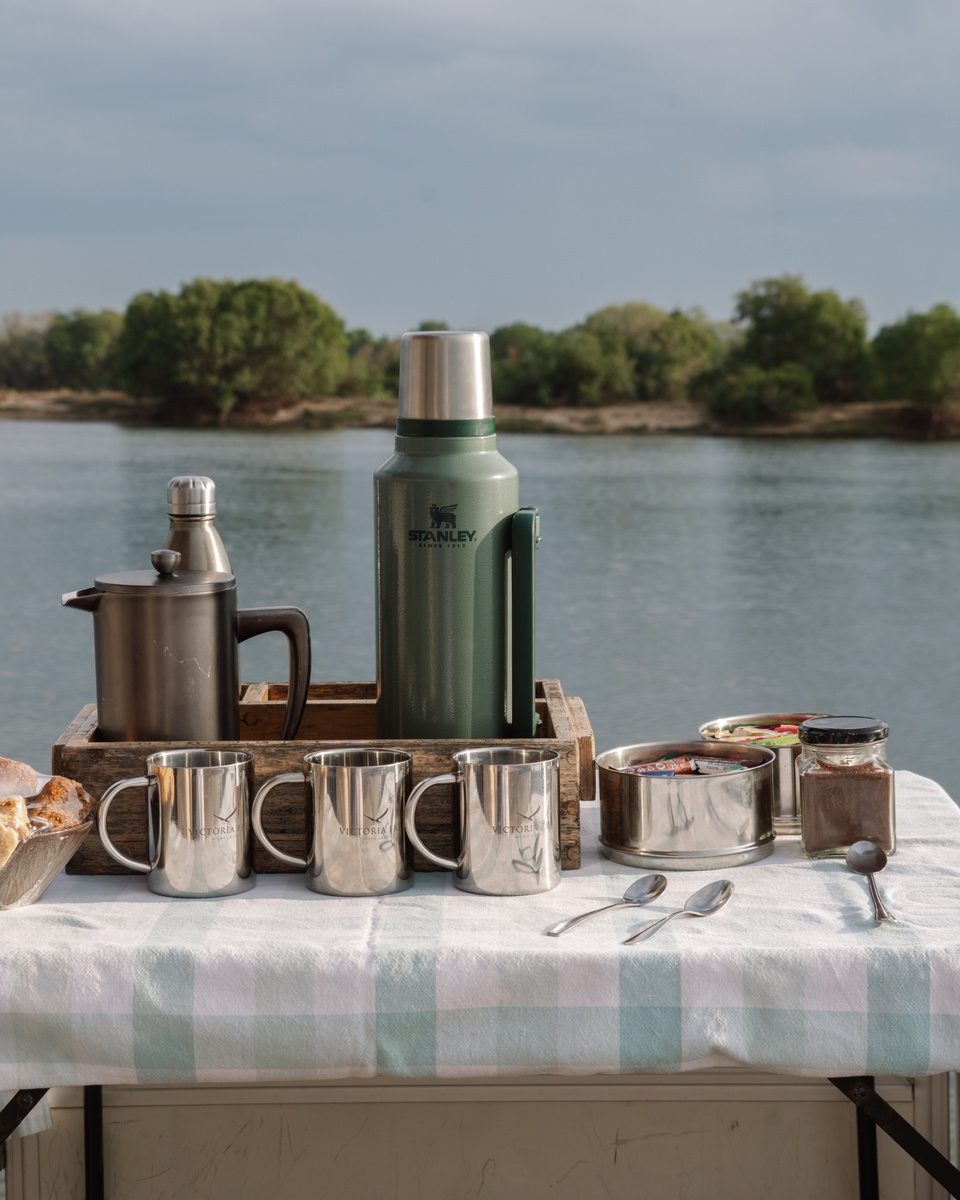 Coffee, metal cups and breakfast pots are arranged beside the Zambezi River at Victoria Falls River Lodge.