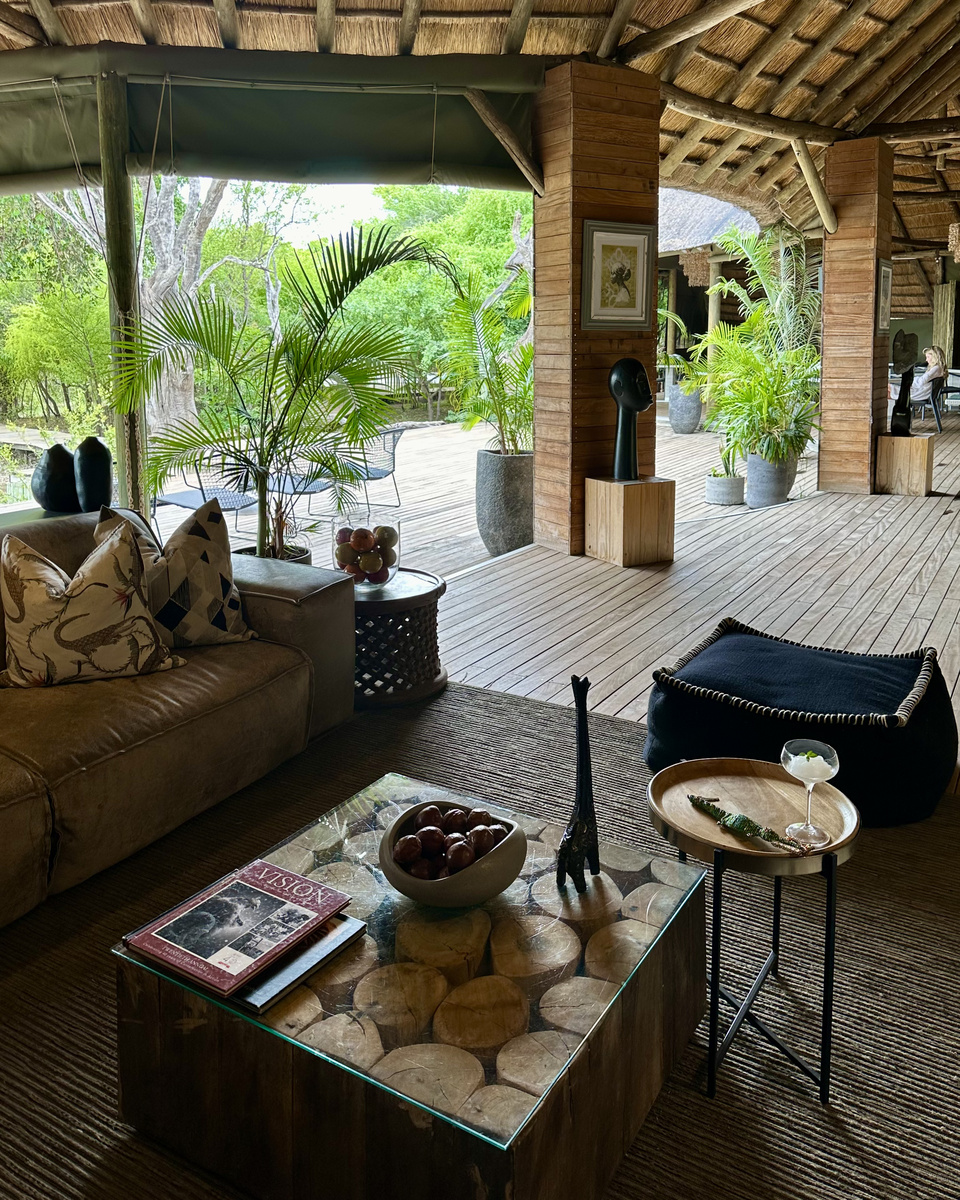 The open-sided lounge at Victoria Falls River Lodge has a leather sofa, sculptural art, greenery and a cocktail set on a brass table.