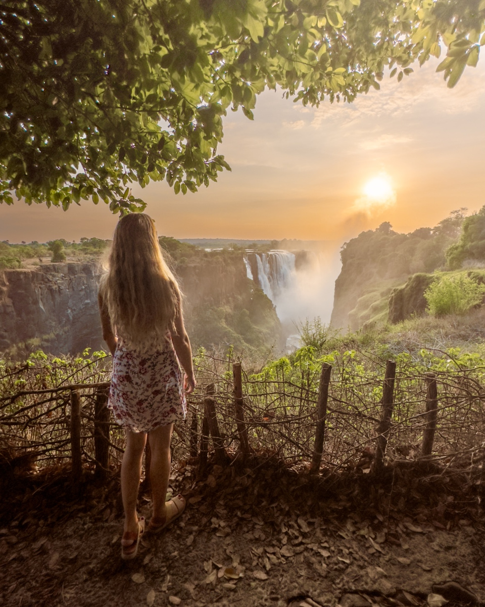 Olga looks across Victoria Falls as the rising sun turns the gorge and river mist gold.