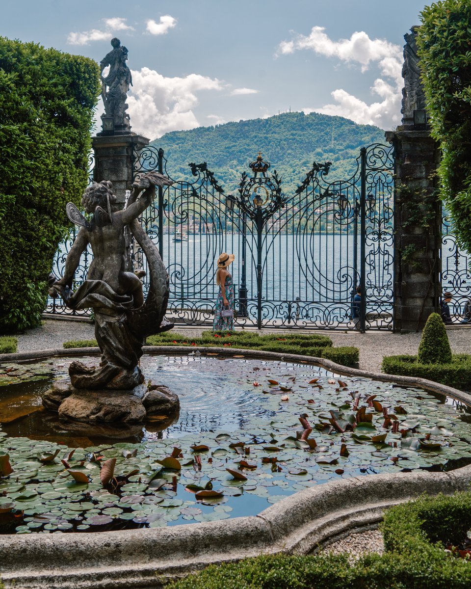 An ornate wrought-iron gate and stone fountain overlook Lake Como in the gardens of Villa Carlotta.