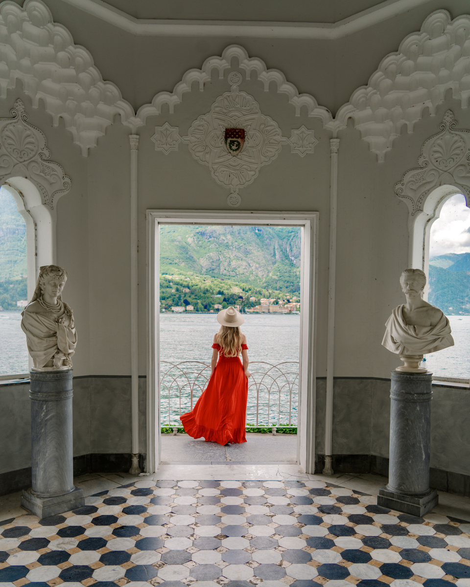 Olga in a red dress looks across Lake Como from the white Moorish kiosk in the gardens of Villa Melzi.