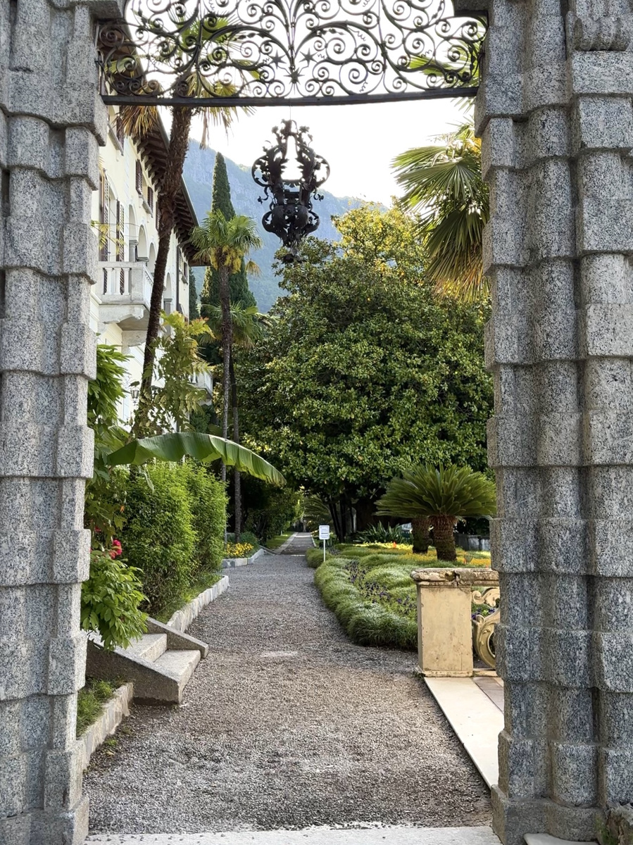 An ornate stone arch and wrought-iron lantern frame a garden path at Villa Monastero.