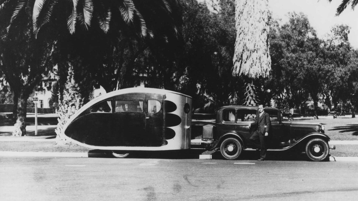 A 1930s automobile towing Wally Byam’s dark streamlined Torpedo Car Cruiser.