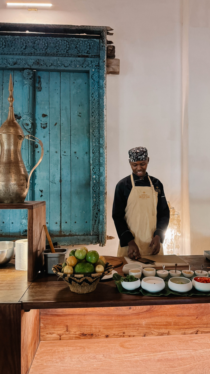 A chef prepares ingredients for a Swahili cooking class beside a carved blue door.