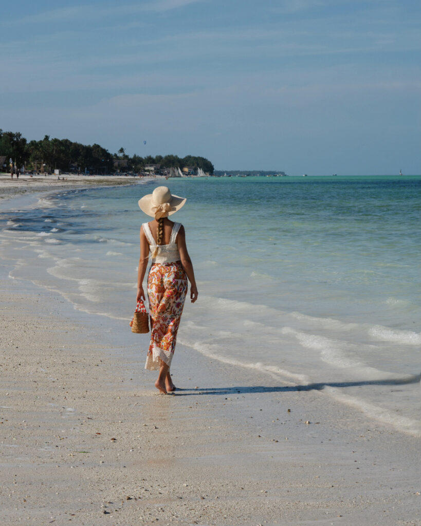 Olga walks along pale Paje Beach beside the turquoise Indian Ocean in Zanzibar.