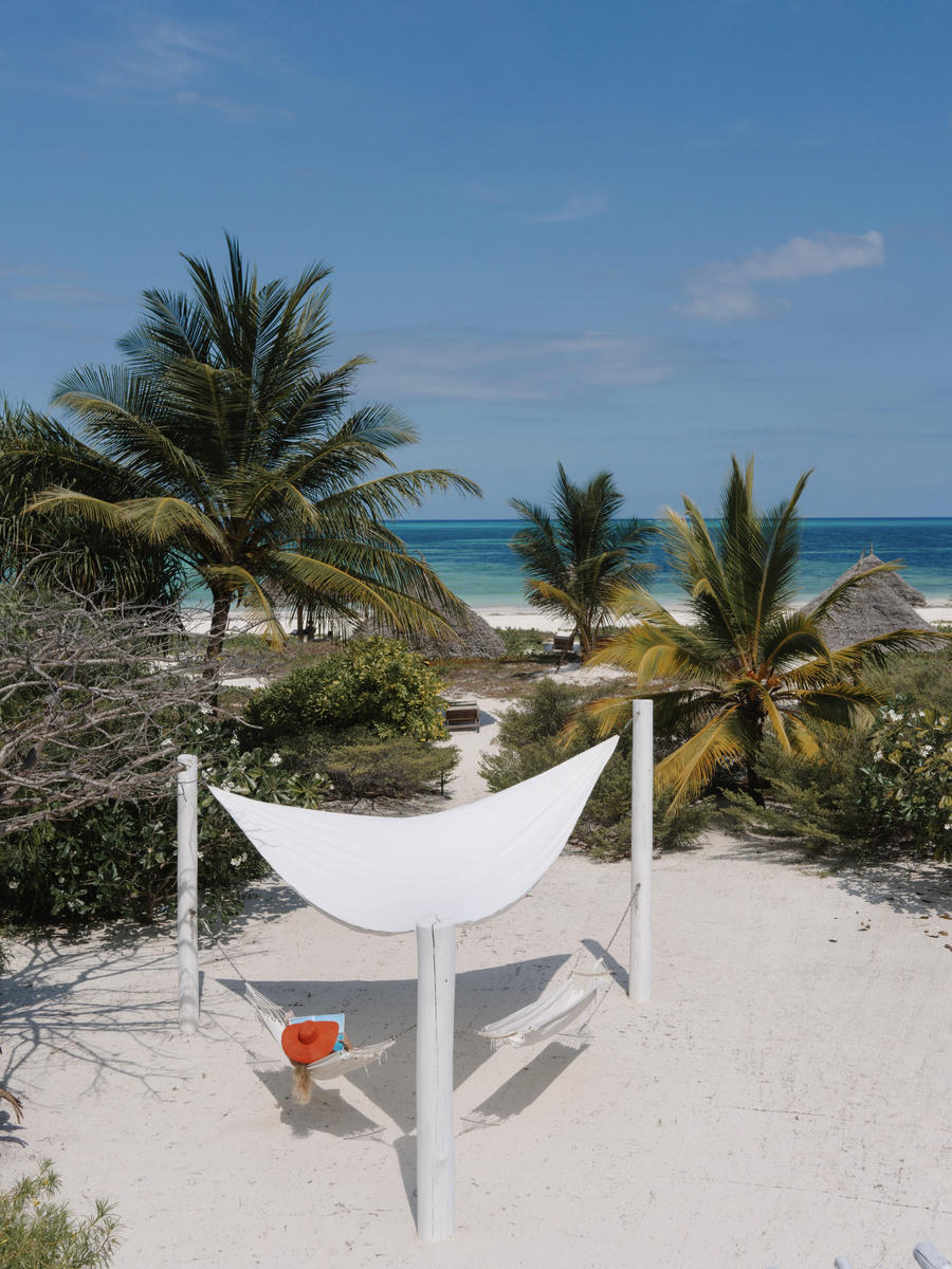 A white hammock in the villa garden overlooks palms, pale sand and the Indian Ocean.