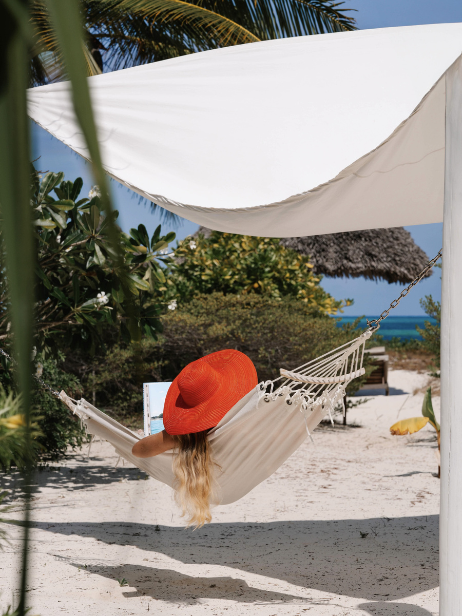 Olga reads in a white hammock in the private garden of her beachfront villa at Zanzibar White Sand.