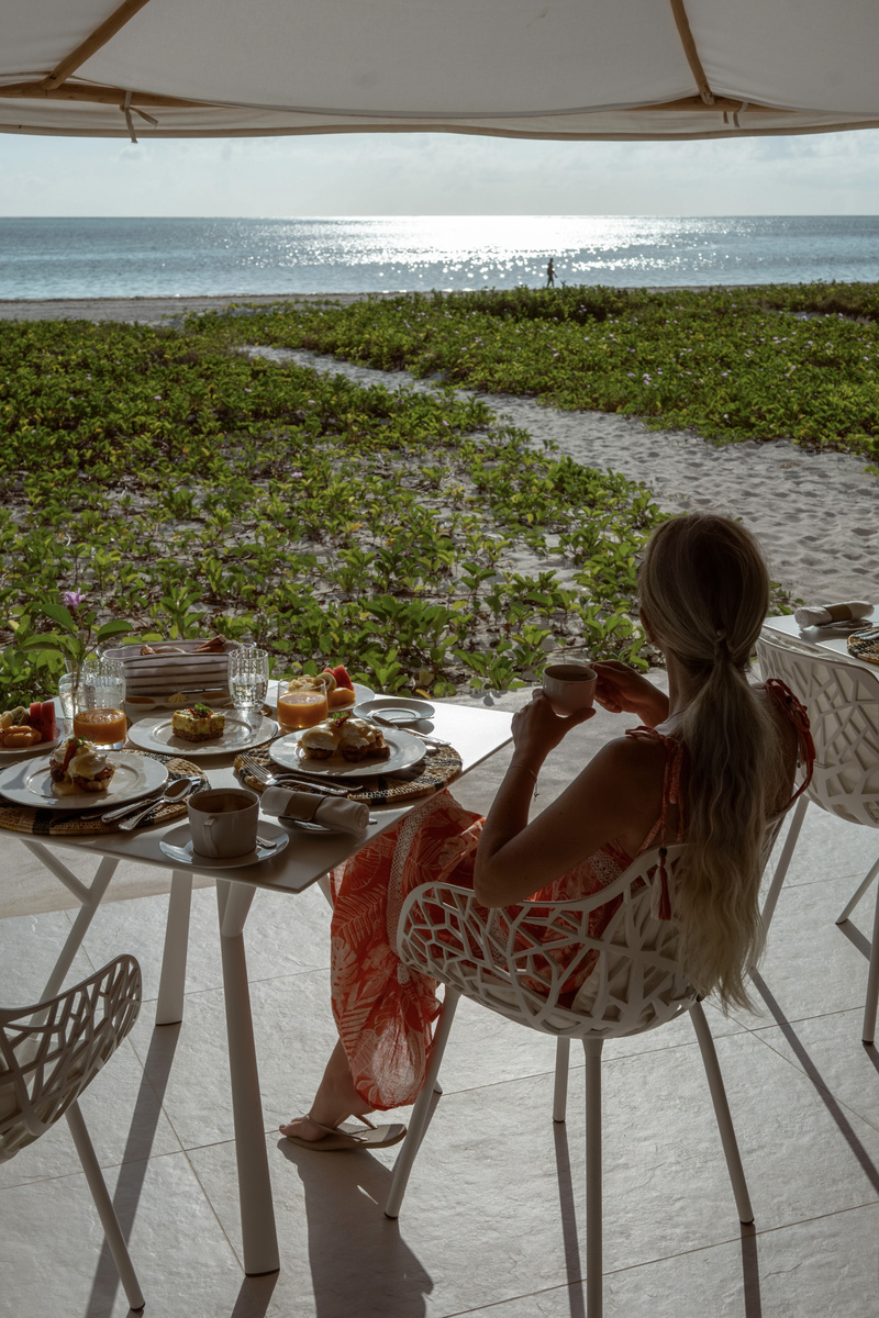 Olga drinks coffee at a breakfast table facing the beach and Indian Ocean.