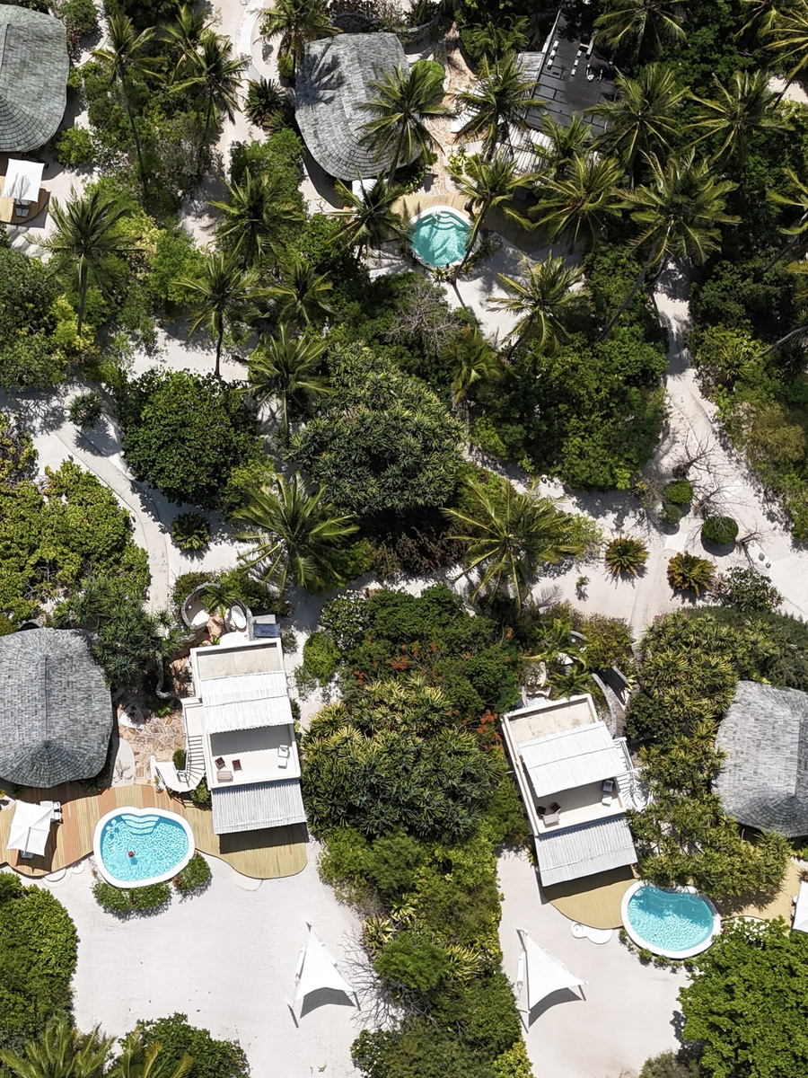 An aerial view shows private pools and villas dispersed through dense tropical gardens.