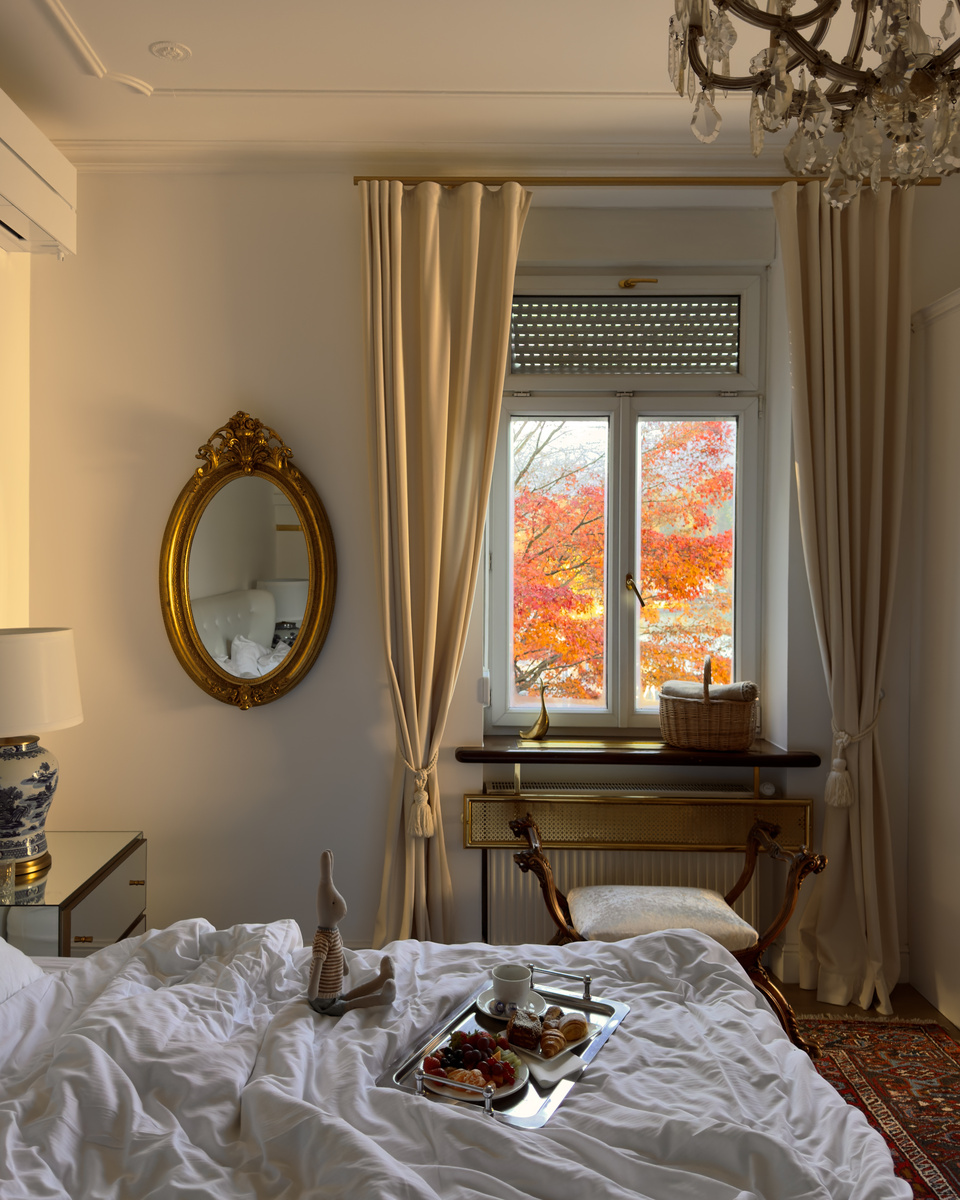 Breakfast trays on the bed beneath a window filled with autumn foliage.