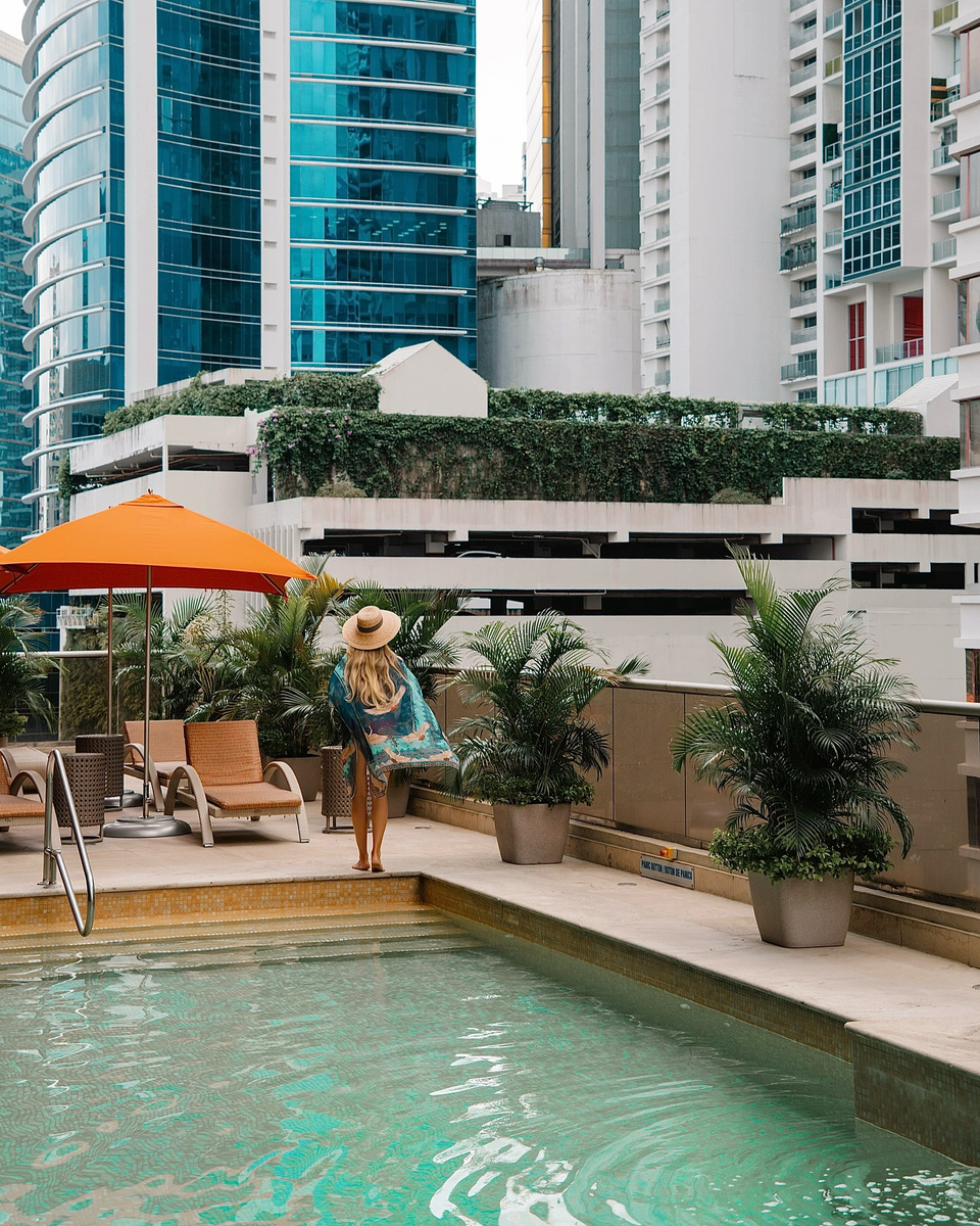 Olga walking beside a rooftop pool among the glass towers of Panama City.