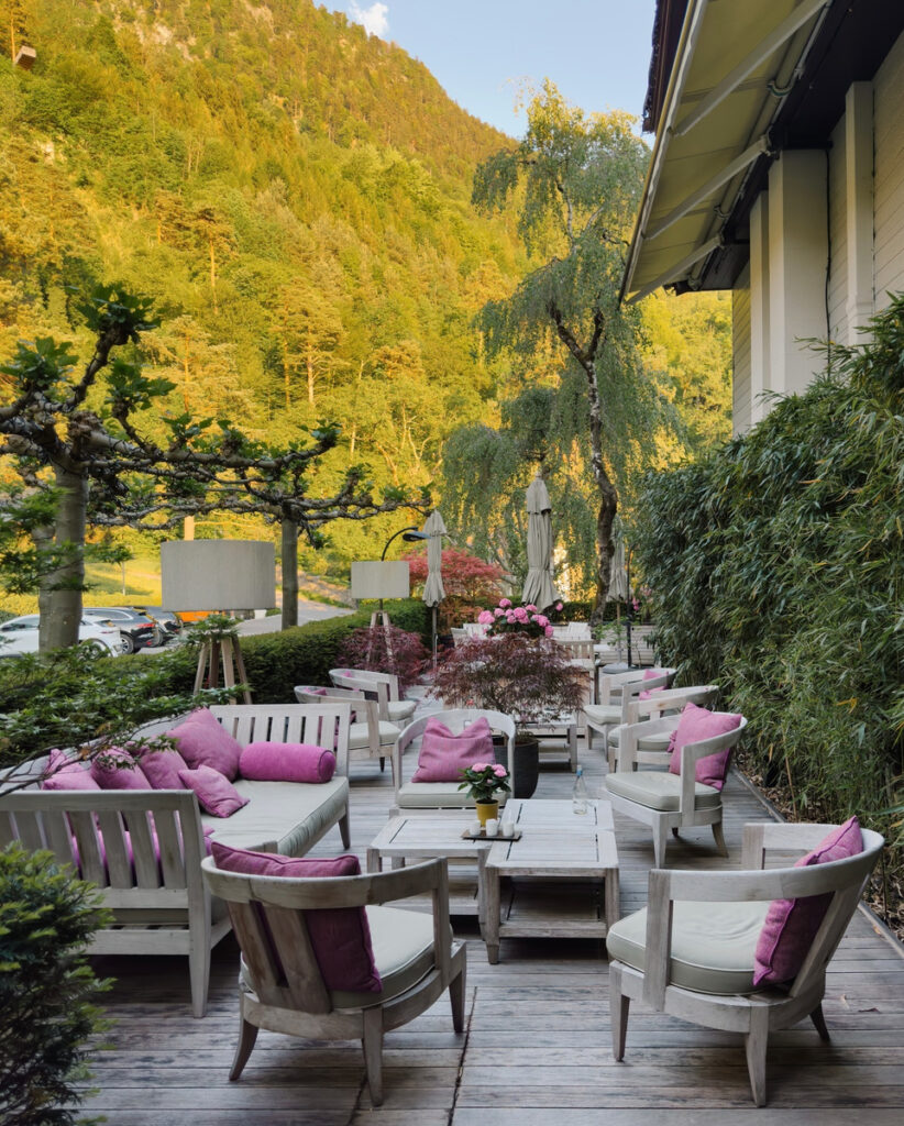 Garden lounge at Park Hotel Sonnenhof, with pale wooden seating below a wooded hillside.