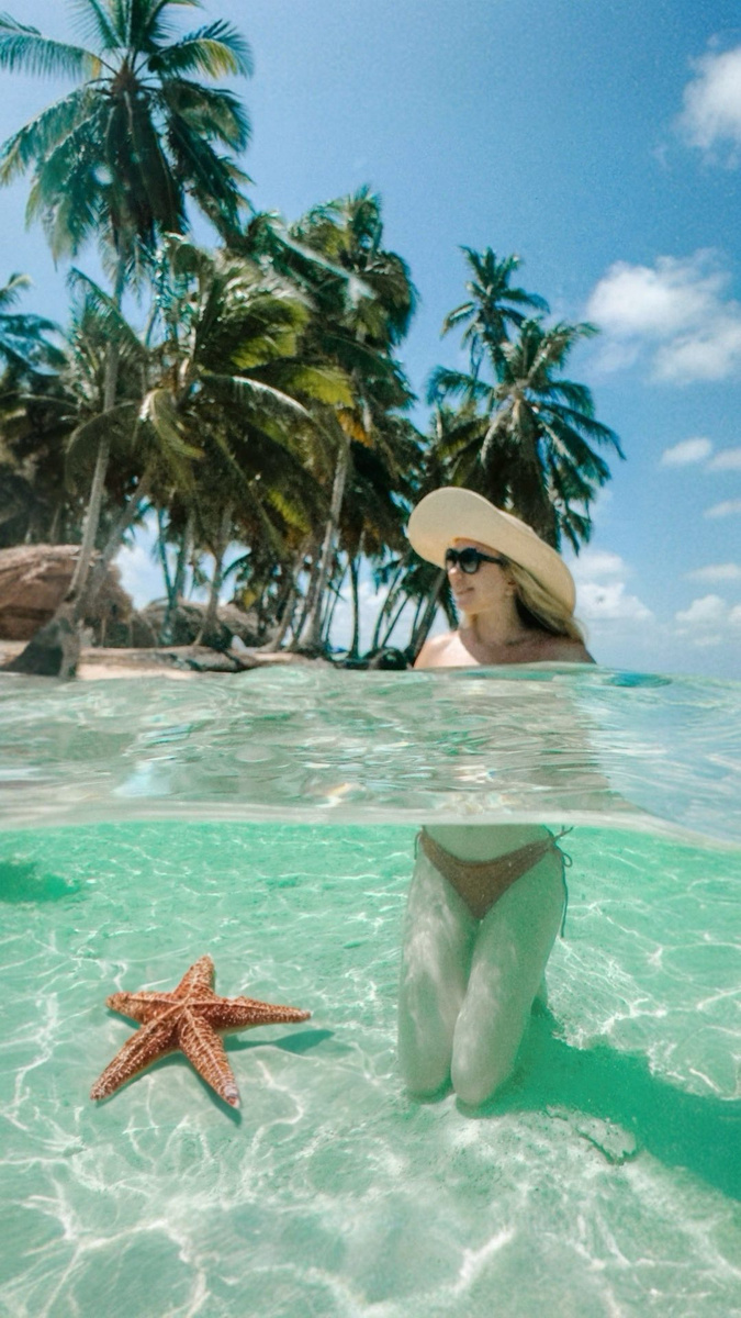 Olga half-submerged in clear Caribbean water beside a starfish, with palms on the shore behind.