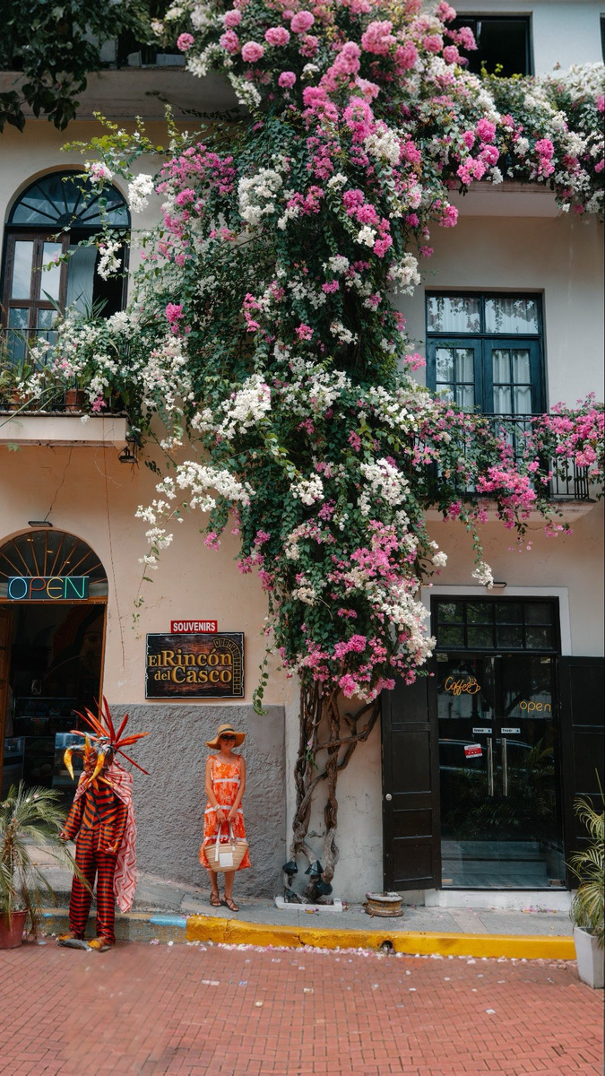 Olga in an orange dress beneath a bougainvillea-draped colonial façade in Casco Viejo, beside a costumed devil figure.