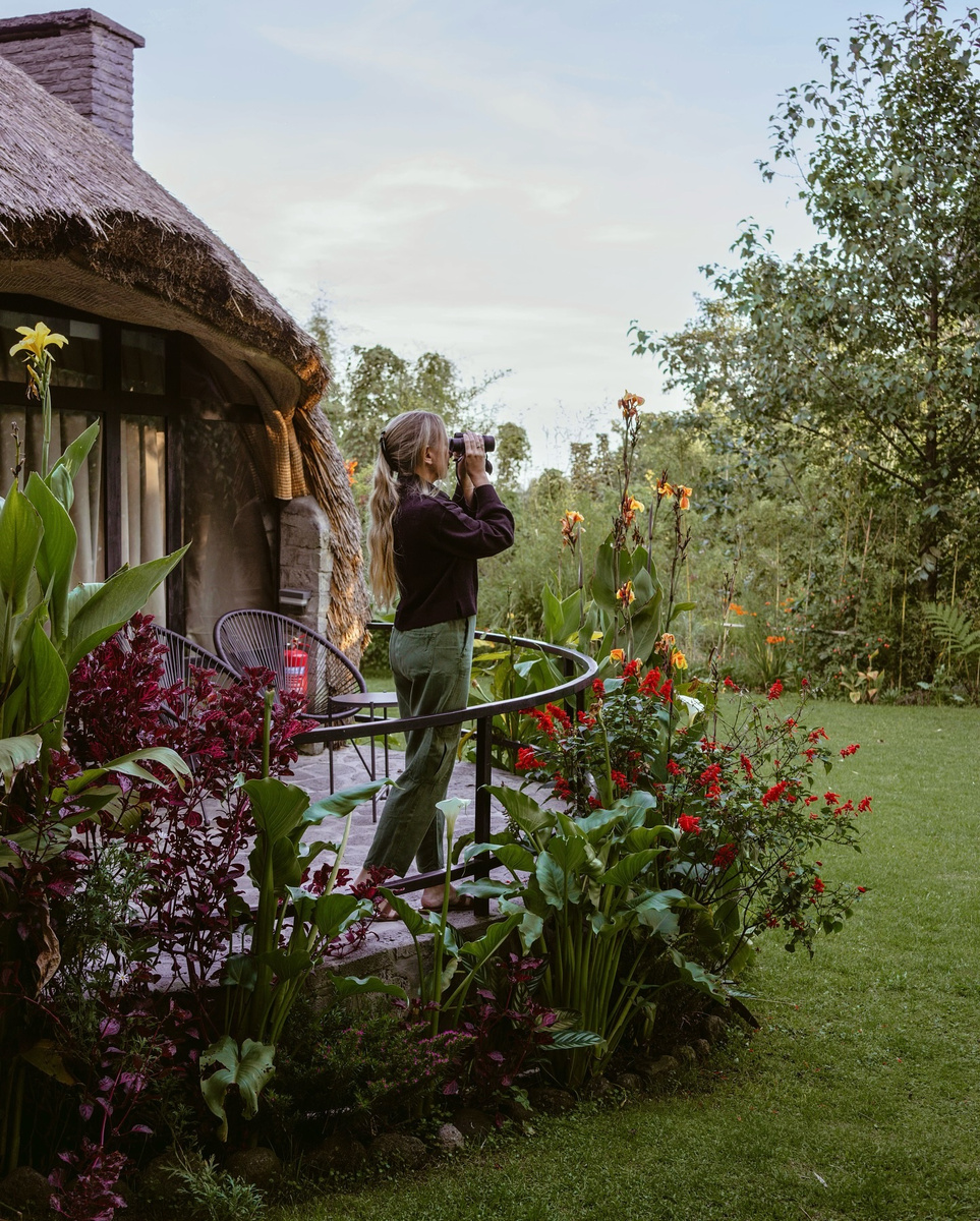 Olga looking through binoculars beside a thatched cottage in Amarembo’s garden in Rwanda.