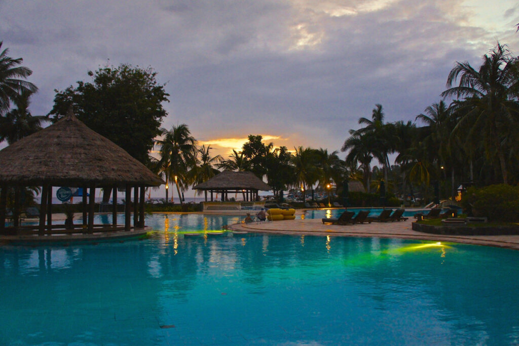 Swimming pool and thatched pavilions at The Santosa Villas & Resort at dusk.