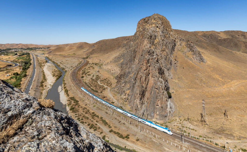 Afrosiyob high-speed train curving through the dry hills beside a narrow river between Jizzax and Gallaorol, Uzbekistan.