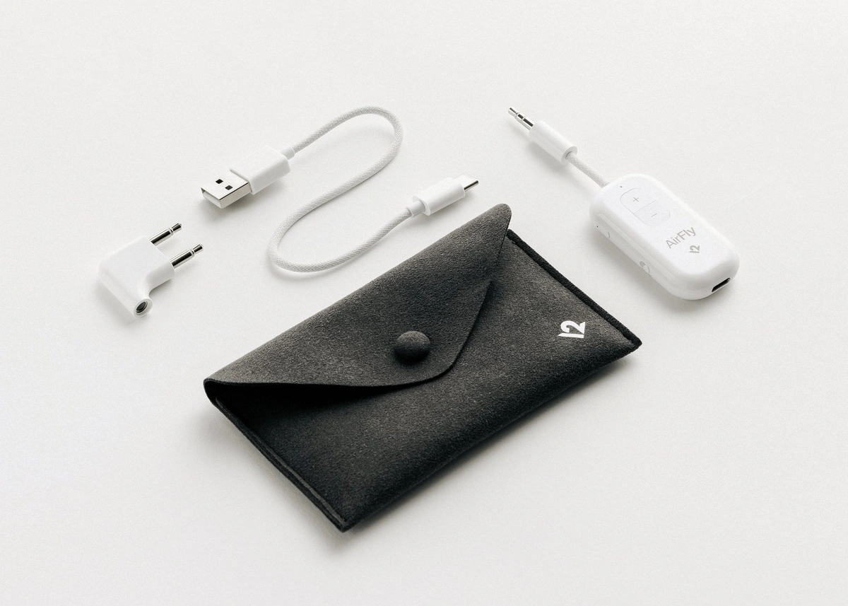 AirFly Pro 2 transmitter, two-pin airline adapter, charging cable and dark travel pouch on a light surface.