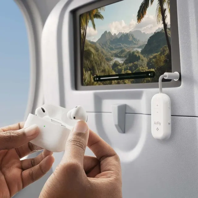 AirFly transmitter connected to an aircraft seatback screen, with hands holding an open AirPods case below.