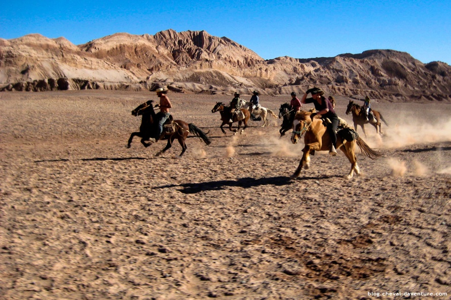 Riders gallop across stony ground beneath bare ridges in the Atacama.