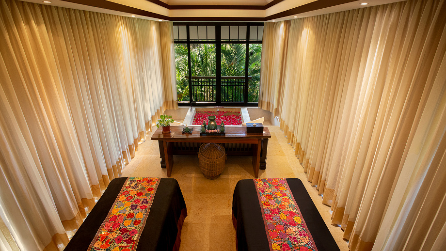 A twin treatment room at Banyan Tree Spa Cabo Marqués, with floral Mexican textile runners and tropical greenery beyond the windows.