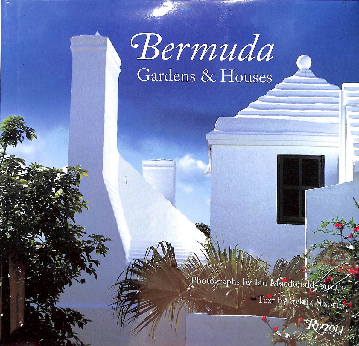 The Bermuda Gardens & Houses cover by Rizzoli, showing a white stepped chimney and whitewashed roof against a deep blue sky, framed by palms and red flowers.