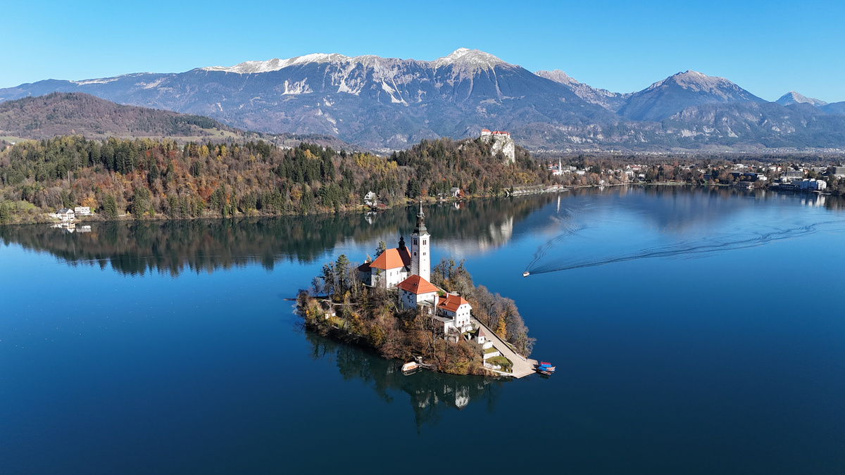 Bled Island reflected in the lake, with the castle and mountains beyond.