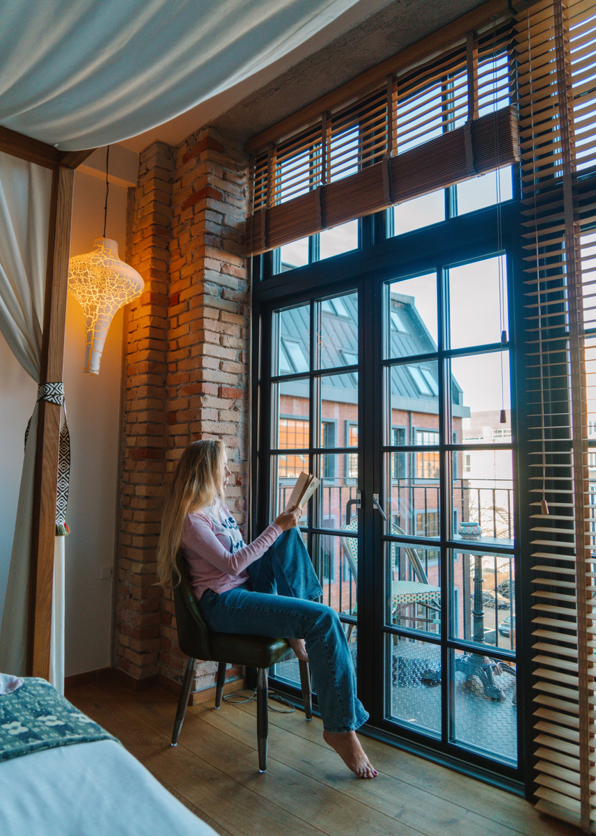 Olga reading beside the balcony doors in a room at Bryggen Guldsmeden