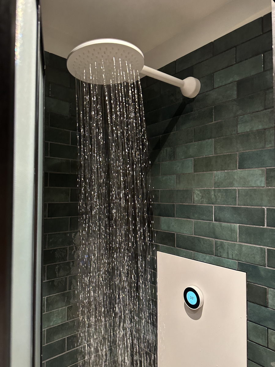Running rainfall shower with a circular digital control in a tiled hotel bathroom
