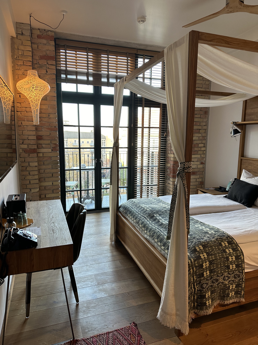 Four-poster bed on the right, a desk on the left and a passage leading to the balcony doors at Bryggen Guldsmeden