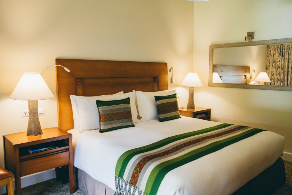 A bed with a wooden headboard, green-striped runner and matching cushions stands between two bedside lamps.