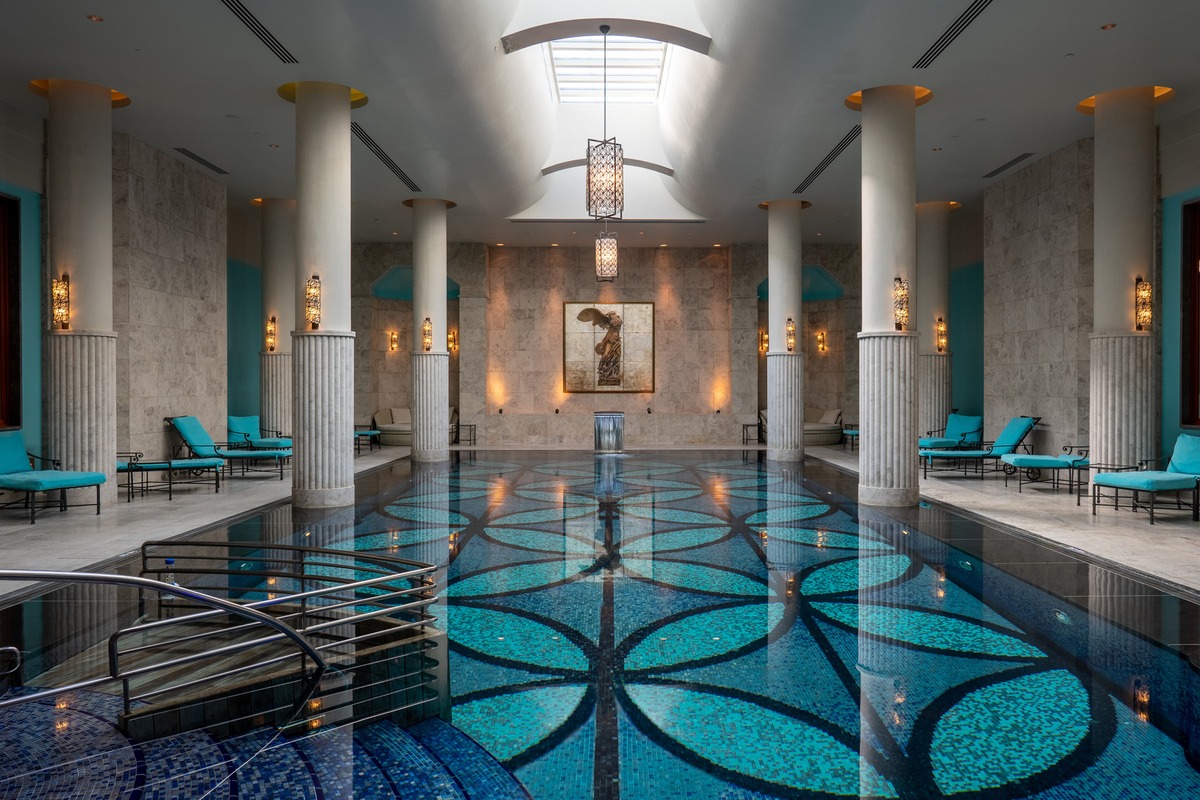 An indoor pool with a blue mosaic floor, stone columns, turquoise loungers and a skylight at Four Seasons Hotel Istanbul at the Bosphorus.