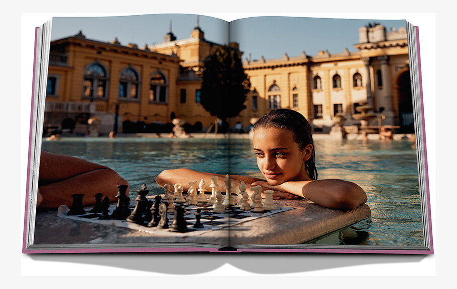 An open spread showing Budapest’s yellow thermal-bath buildings and a woman beside a floating chessboard.