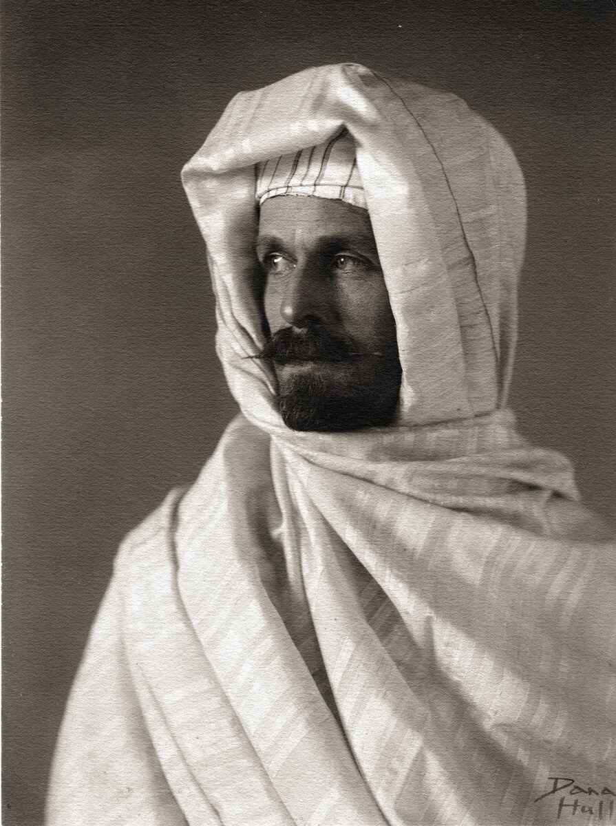 Burton Holmes wrapped in pale Moroccan robes and a hooded headcloth, looking to one side.