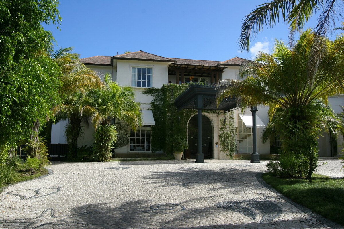 Casa Colonial’s two-storey entrance façade framed by palms beside a cobbled driveway